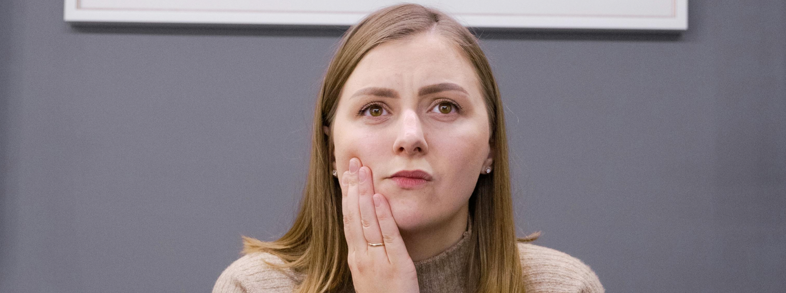 Eine Frau mit Schmerzen wegen einer Zahnfleischbluten hält sich die Wange.