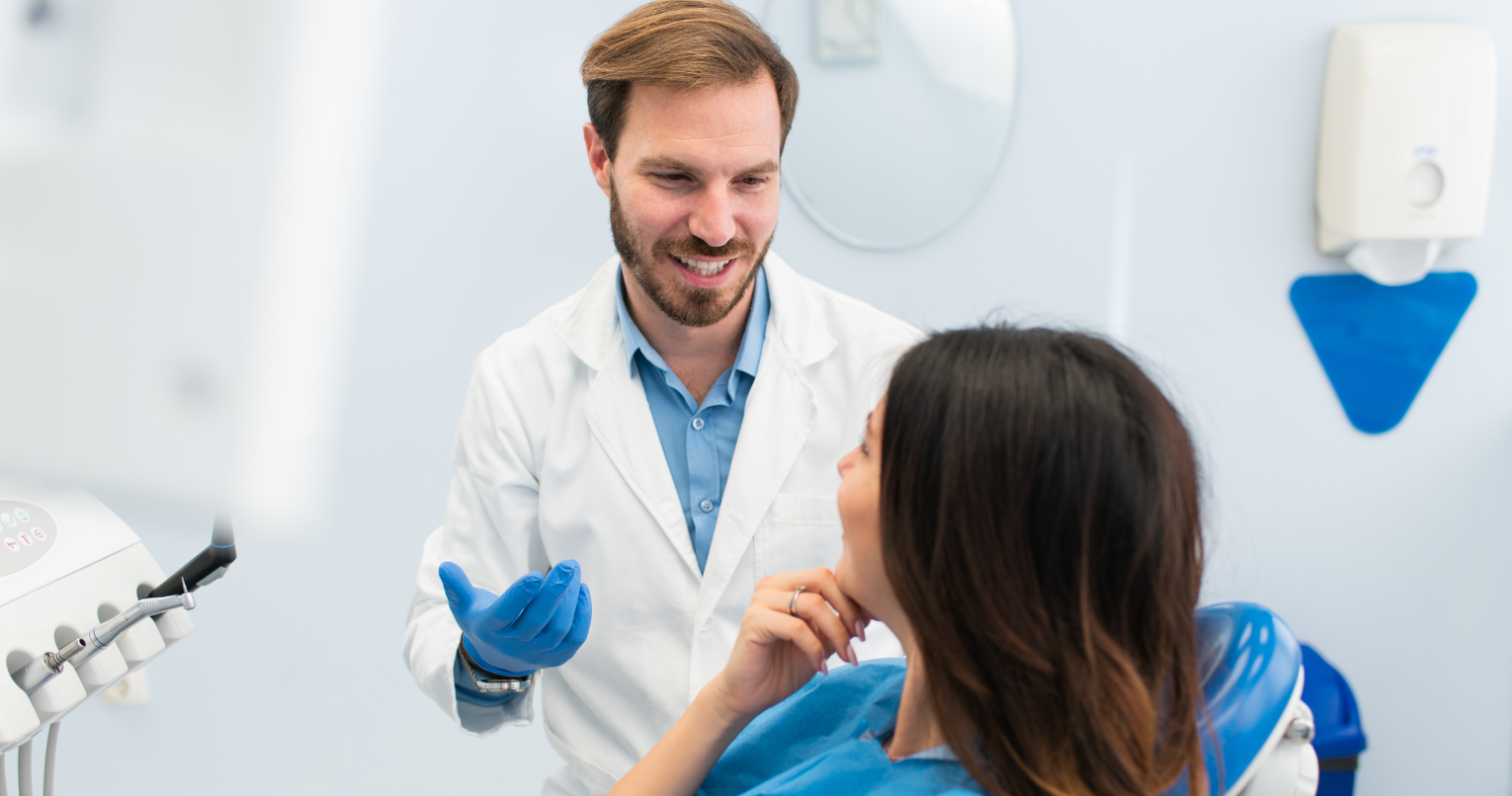 Ein Zahnarzt behandelt eine Patientin und lächelt dabei.
