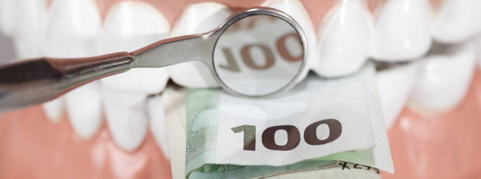 Eine Zahnprothese, die auf einen 100-Euro-Schein beißt.