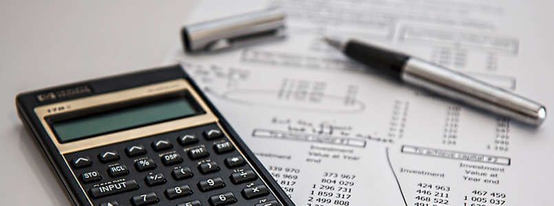 Zu sehen ist ein Taschenrechner auf einer Rechnung, um darzustellen, wie hoch Zahnersatz Kosten ausfallen können.