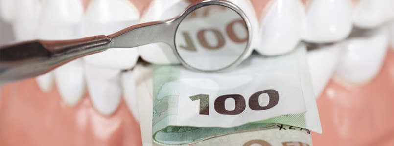 Zu sehen sind Geldscheine in einem Gebiss, um darzustellen, dass Zahnimplantat Kosten schnell sehr hoch werden können.