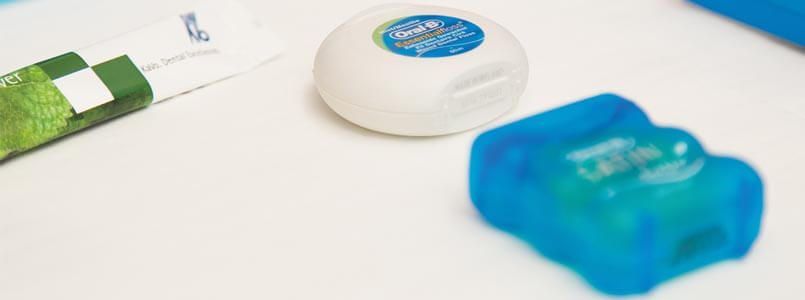 Zahnseide und weitere Hilfsmittel zur täglichen Zahnreinigung liegen auf einem Tisch.