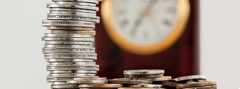 Ein Stapel Münzen vor einer Uhr