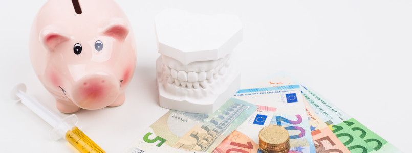 Ein Modell eines Gebisses umringt von Geld und einem Sparschwein.