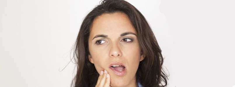 Eine Frau mit Zahnschmerzen fasst sich an die Wange.