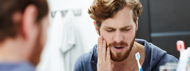 Ein Mann der Zahnschmerzen beim Zähneputzen verspürt.