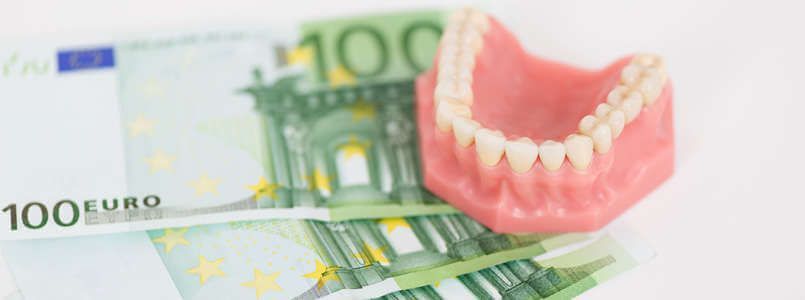 Zu sehen ist ein Gebiss auf Geldscheinen, um zu zeigen, dass bei Zahnarztkosten große Preisunterschiede entstehen können.