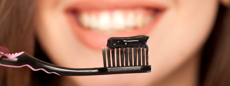 Eine Frau putzt sich mit schwarzer Aktivkohle die Zähne.