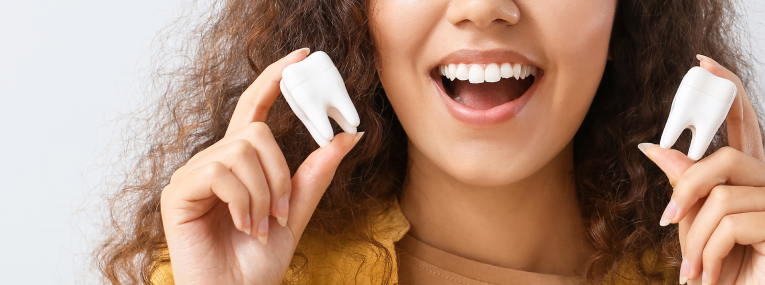 Zu sehen ist eine Frau mit Modellen eines Zahnes, um zu zeigen, was bei der Zahnimplantat-Pflege beachtet werden muss.