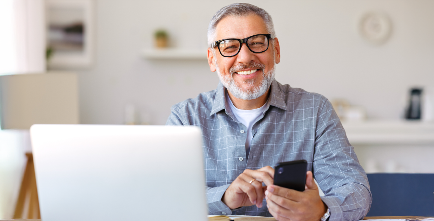 Ein Mann informiert sich am Laptop und Handy über die Laufzeit einer Zahnzusatzversicherung.