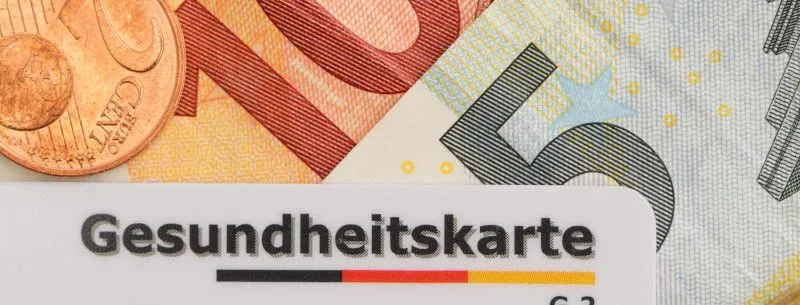 Zu sehen ist eine Krankenkassenkarte auf Geldscheinen, die zeigen sollen, wie hoch die Kostenübernahme der Krankenkasse ist.