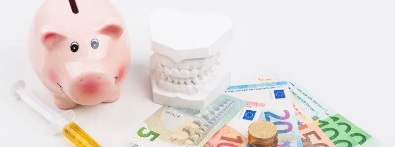 Ein Modell eines Gebisses umringt von Geld und einem Sparschwein.