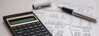 Zu sehen ist ein Taschenrechner auf einer Rechnung, um darzustellen, wie hoch Zahnersatz Kosten ausfallen können.