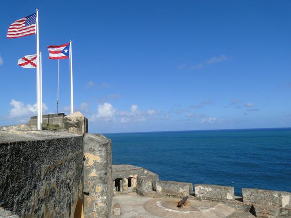 Photo of flags waving against a blue sky at Castillo San Felipe del Morro in San Juan, Puerto Rico.