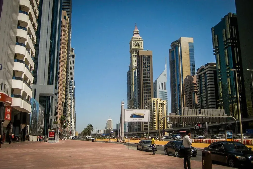 High-rise towers along a main road in Dubai under a clear sky.