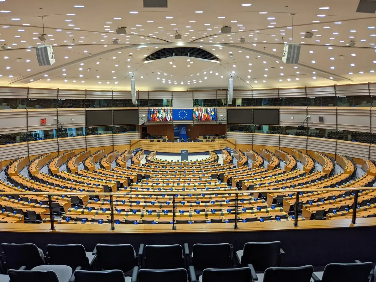 The empty plenary chamber of the European Parliament in Brussels, with the EU flag and member-state flags behind the podium.