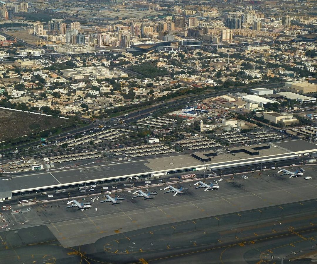 Vista aérea de la Terminal 2 del aeropuerto internacional de Dubái, con aviones en las puertas de embarque y la ciudad al fondo.