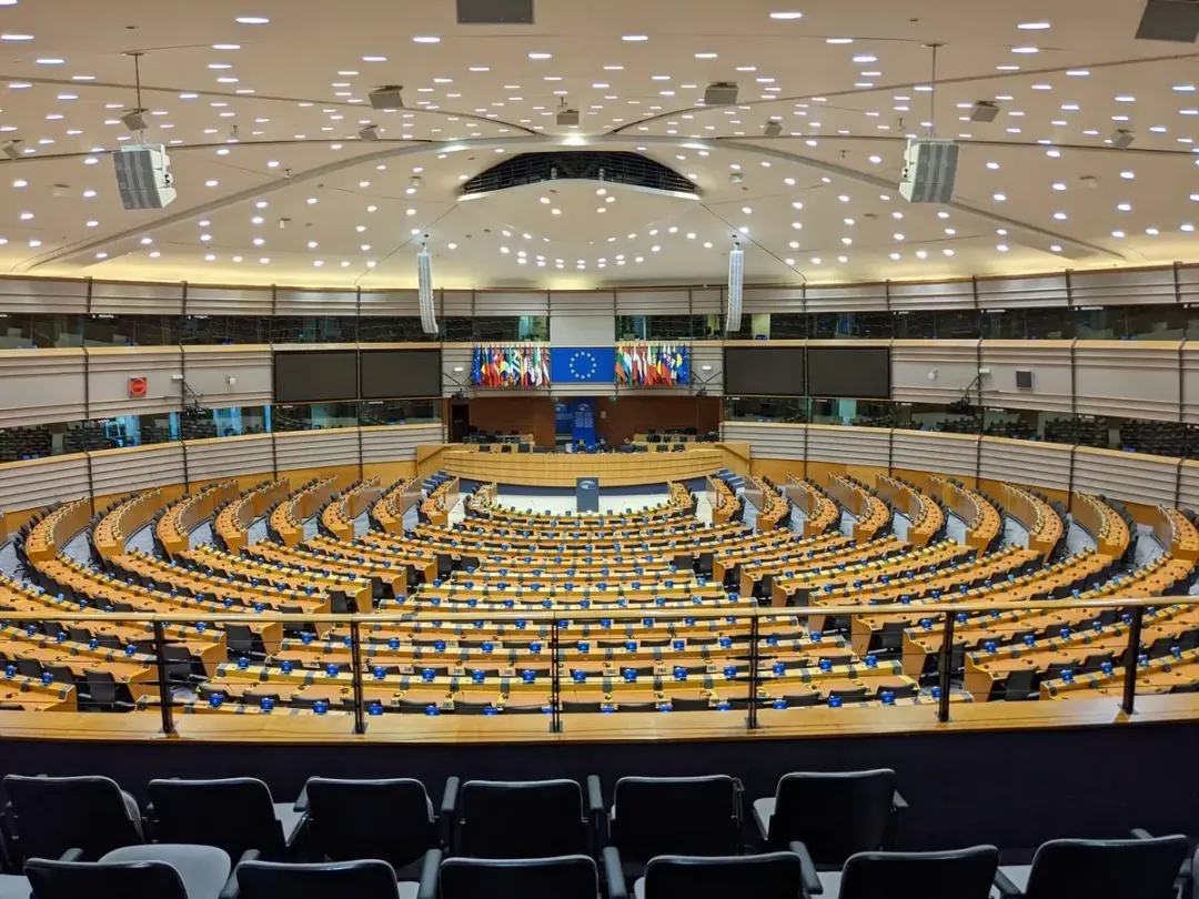 The empty plenary chamber of the European Parliament in Brussels, with the EU flag and member-state flags behind the podium.