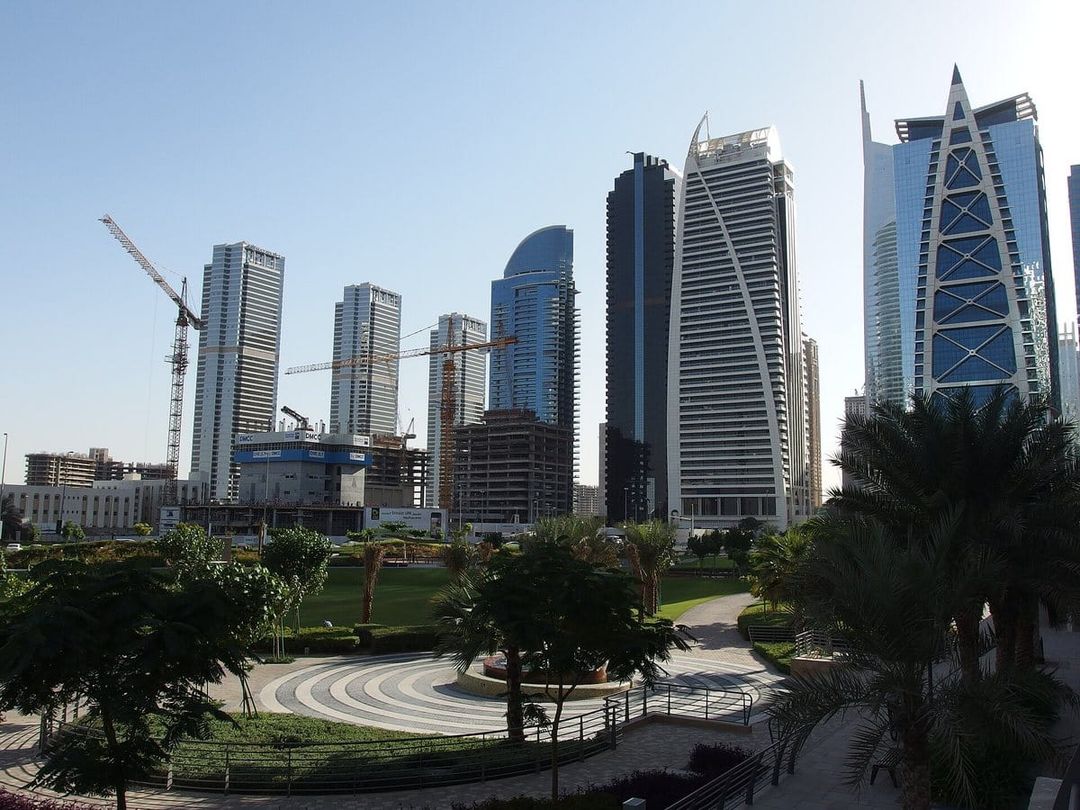 Torres residenciales de Jumeirah Lakes Towers vistas desde un parque con palmeras y césped.