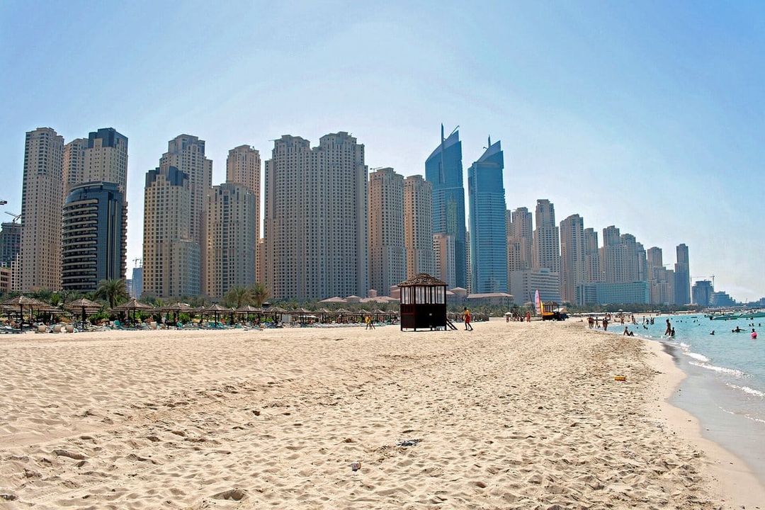 Arena de la playa de Jumeirah Beach Residence con sombrillas, frente a una hilera de torres residenciales.