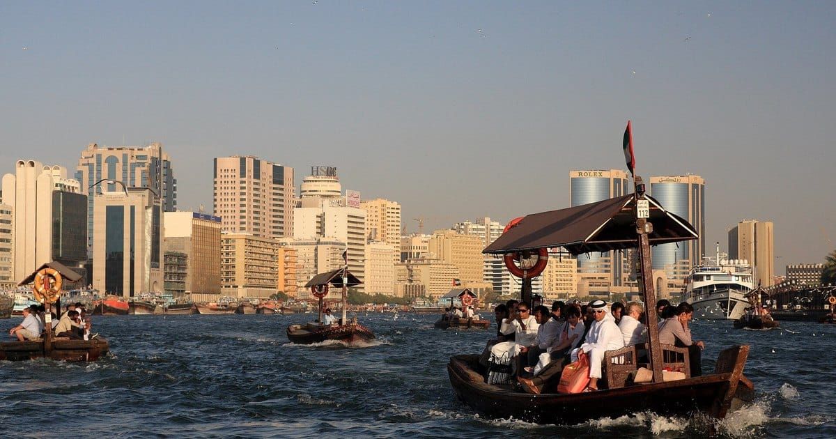 Abras en bois chargées de passagers traversant la crique de Dubaï, devant les immeubles de bureaux de Deira, dans la lumière de fin d'après-midi.