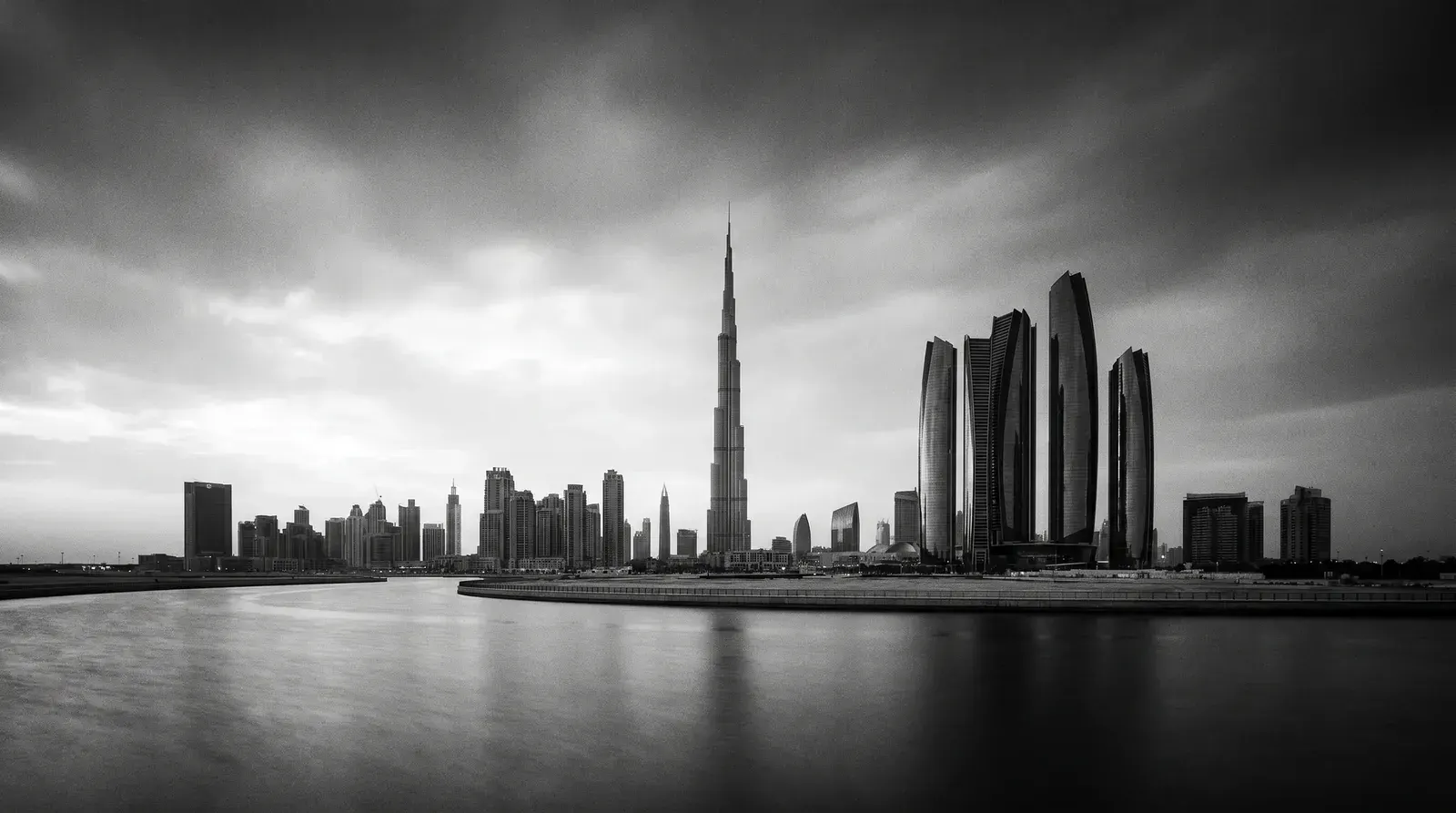 Black-and-white Dubai skyline with the Burj Khalifa and Downtown towers reflected in still water
