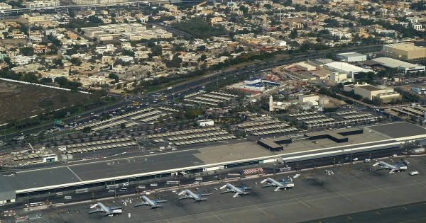 Vue aérienne du terminal 2 de l'aéroport international de Dubaï, avec des avions stationnés sur l'aire de trafic et des quartiers résidentiels en arrière-plan.