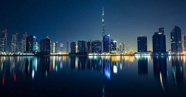 Die Skyline von Business Bay in Dubai mit dem Burj Khalifa spiegelt sich bei Nacht im Wasser.