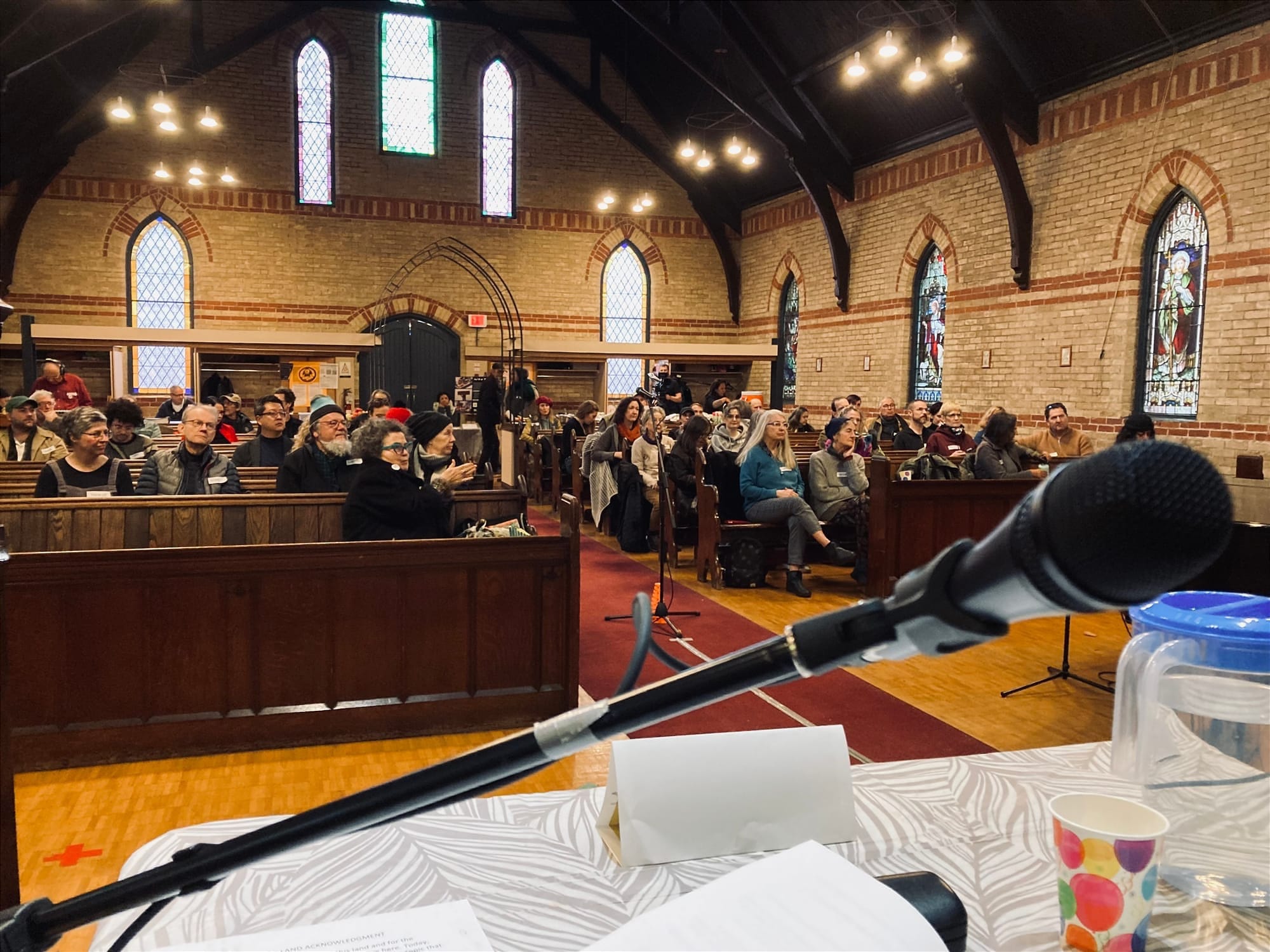 Viewed from the stage, a large group of artists and arts workers fill the pews in a historic neighbourhood church.