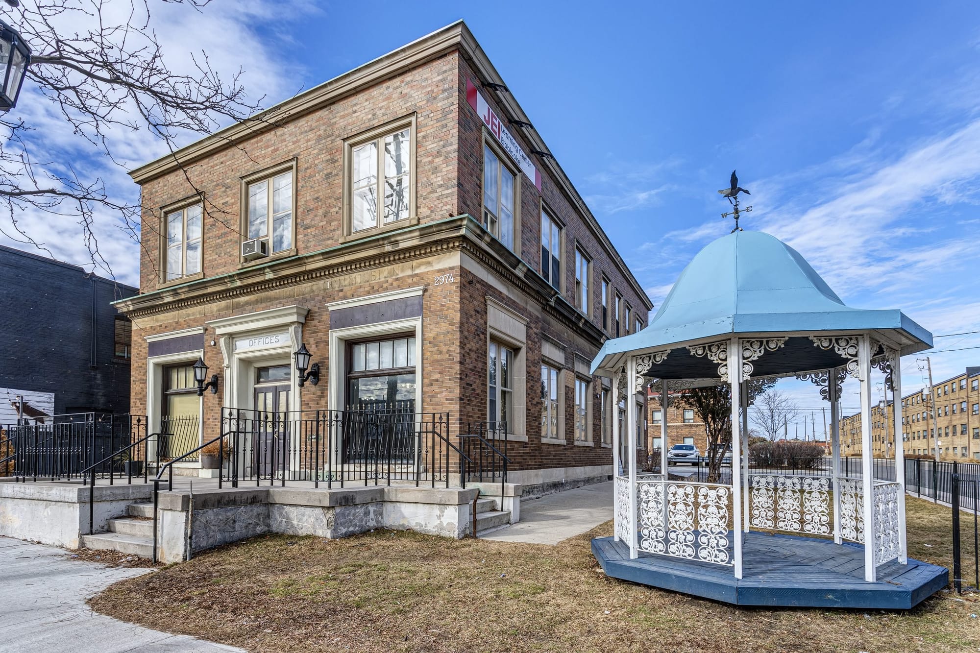 A tan two-storey heritage building beside a yard with a blue and white gazebo.