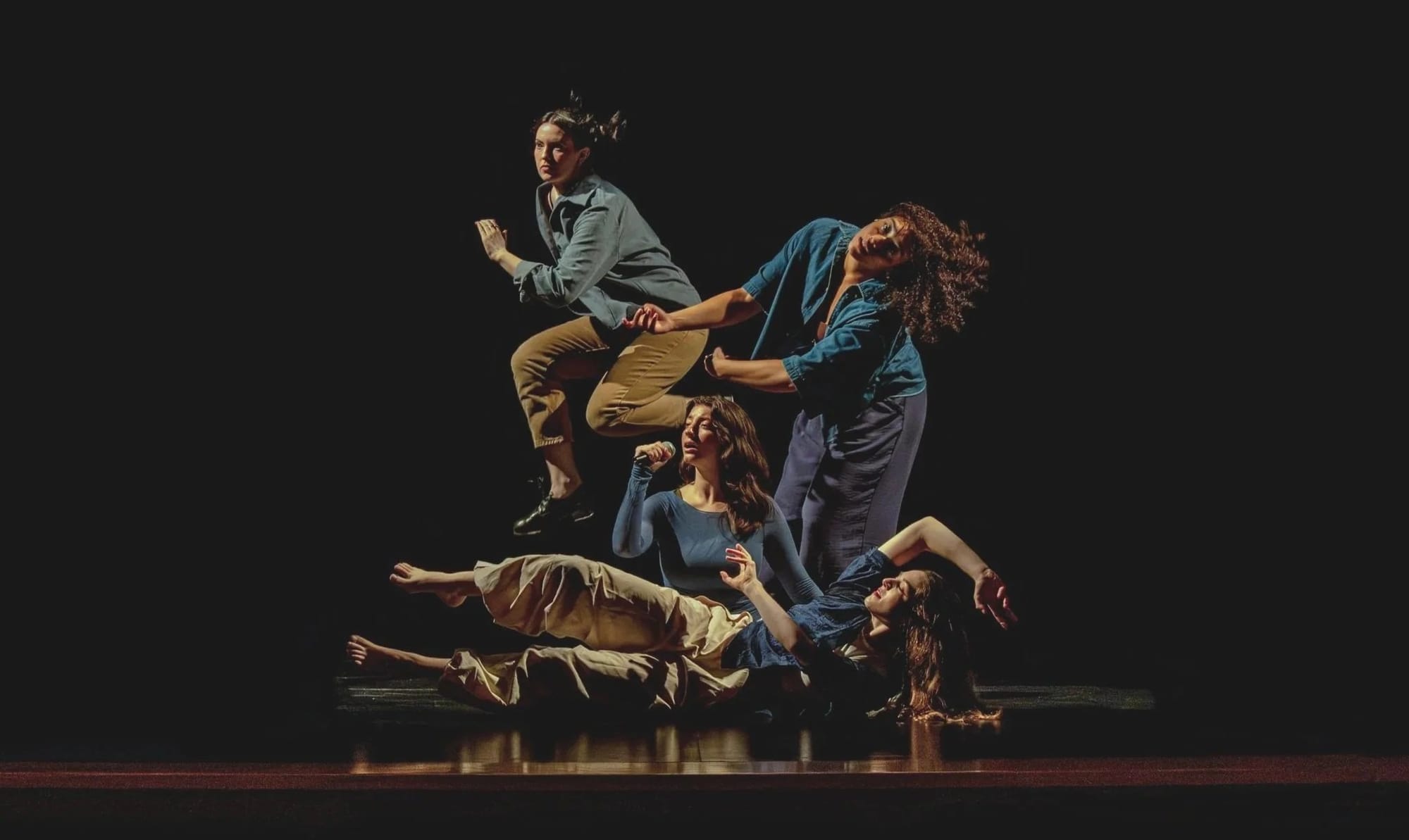 Four dancers in quasi-pyramid formation on a darkened stage.