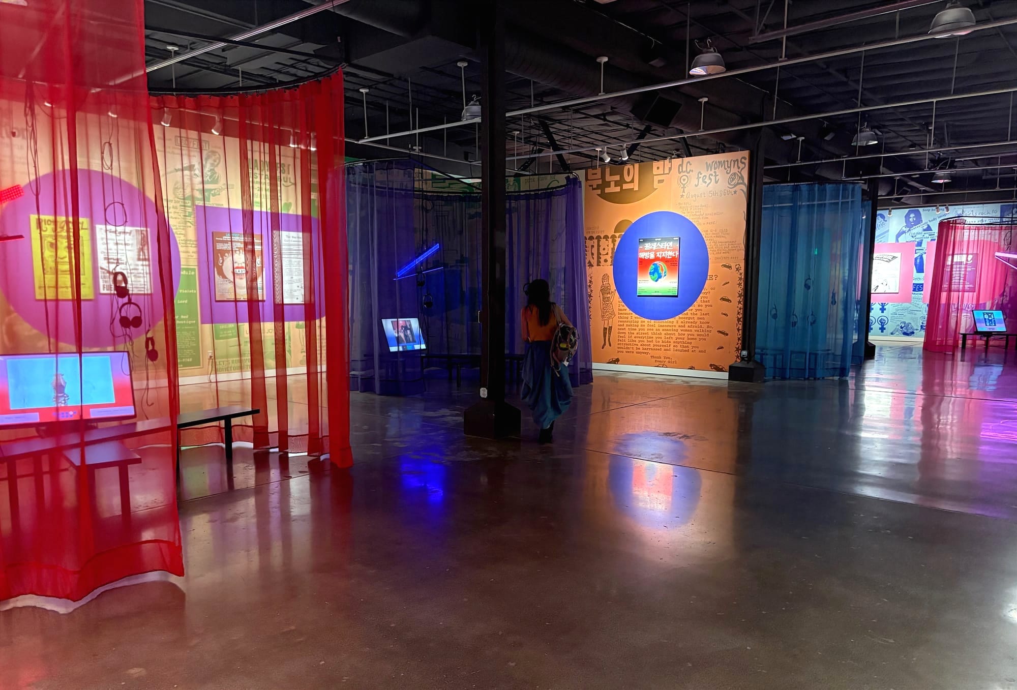 A large art gallery space partitioned by gauzy curtains, with posters and other historical artifacts on display. 