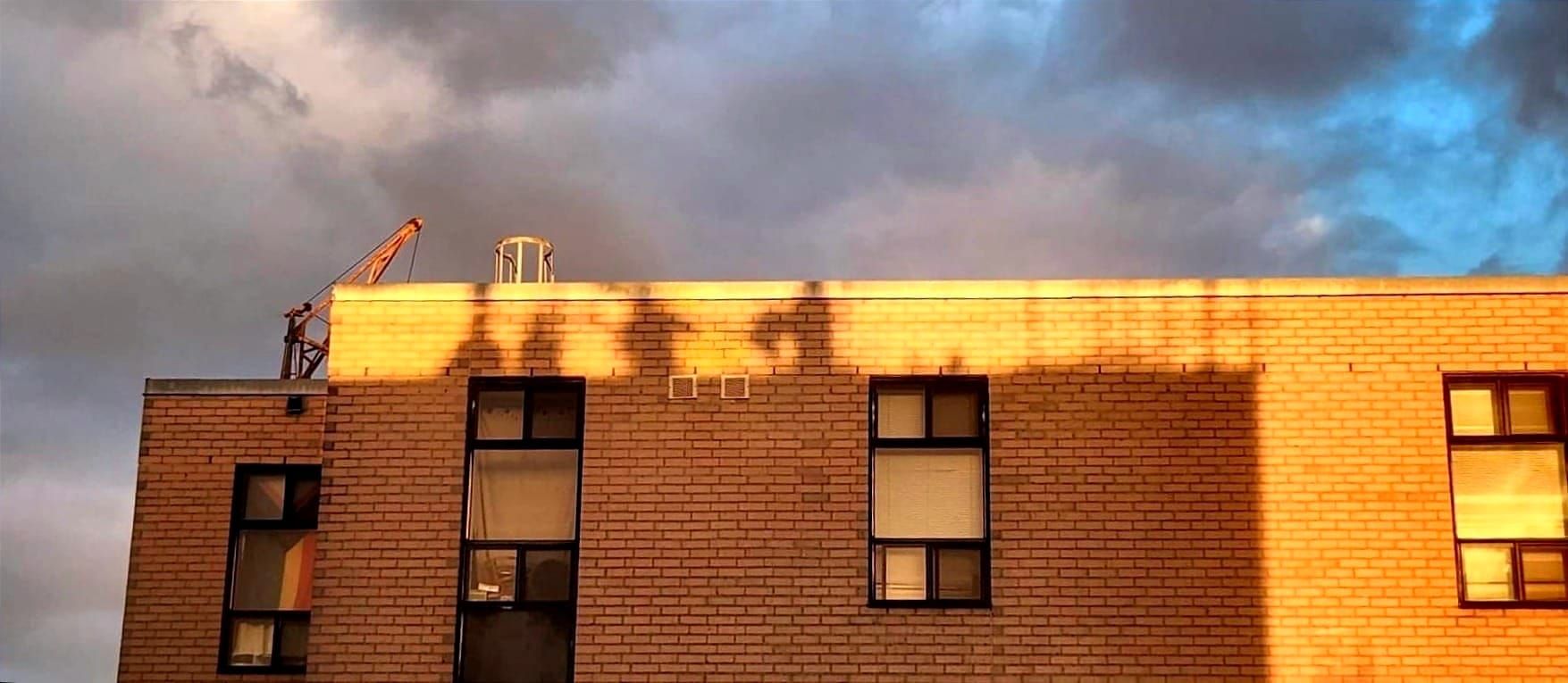 A photograph of M3 with the shadows of roof workers on M2, with a backdrop of a moody sky.