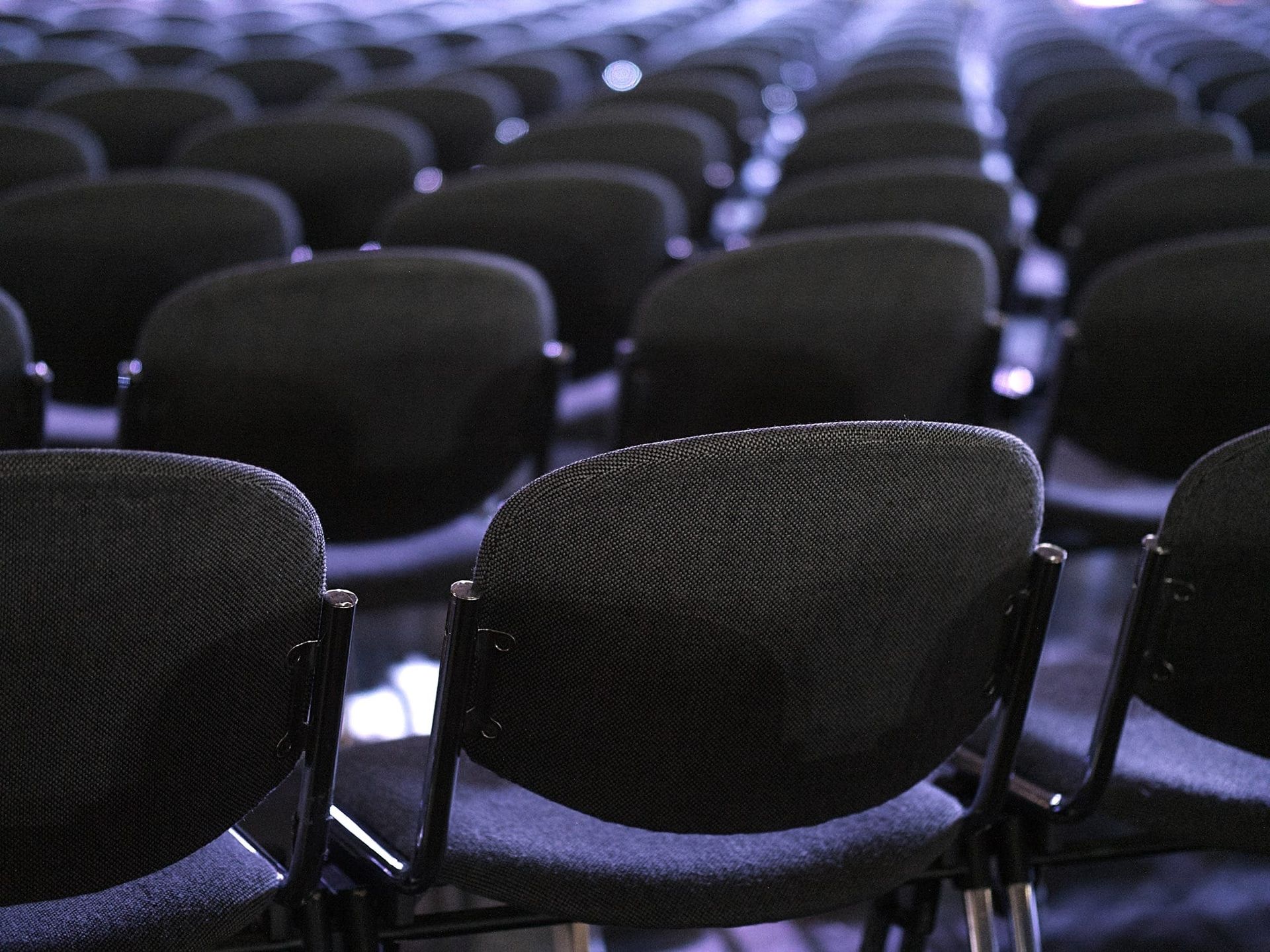 Rows of grey chairs in a darkened meeting hall.