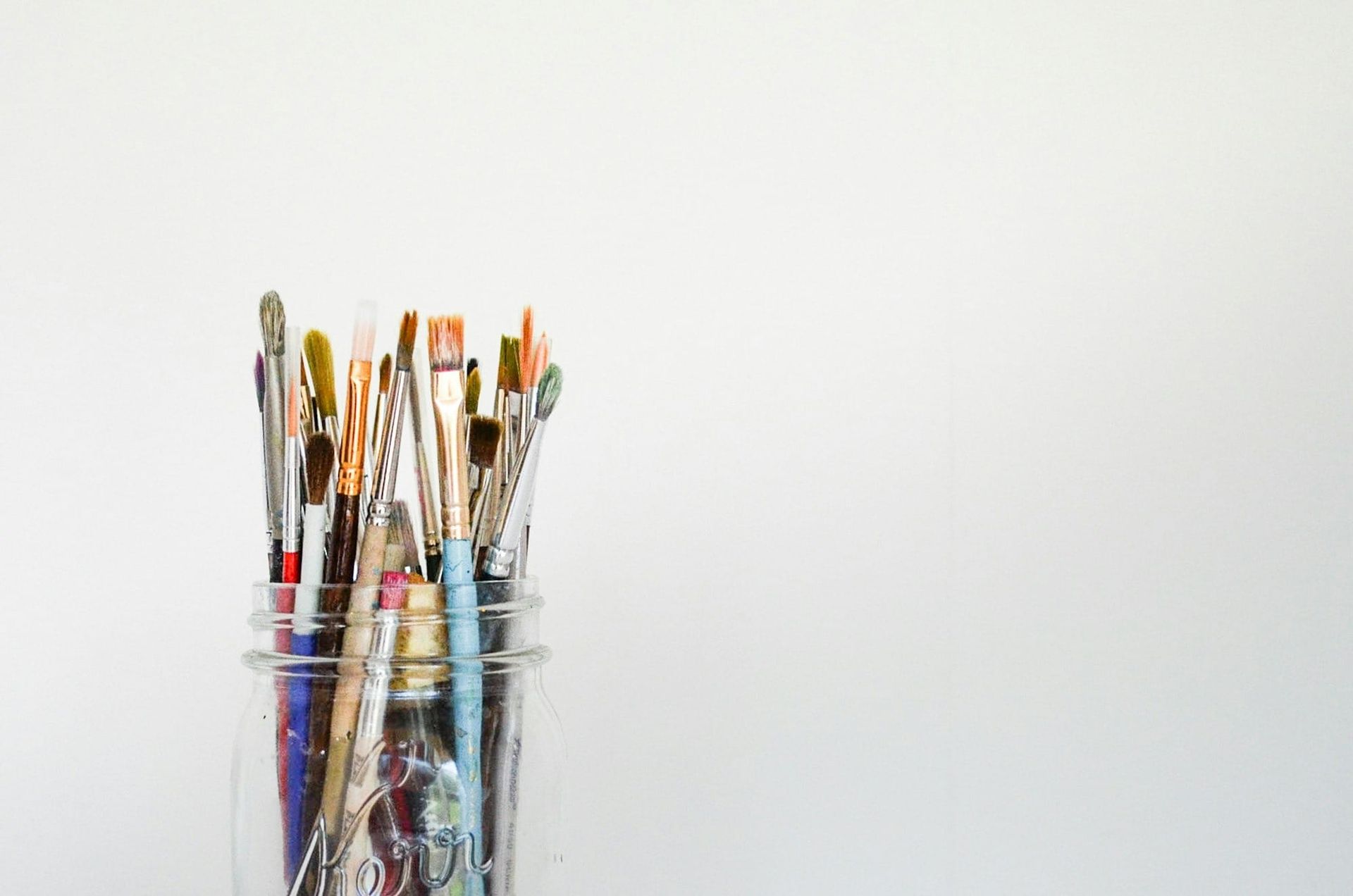 A mason jar filled with paint brushes against a white background.