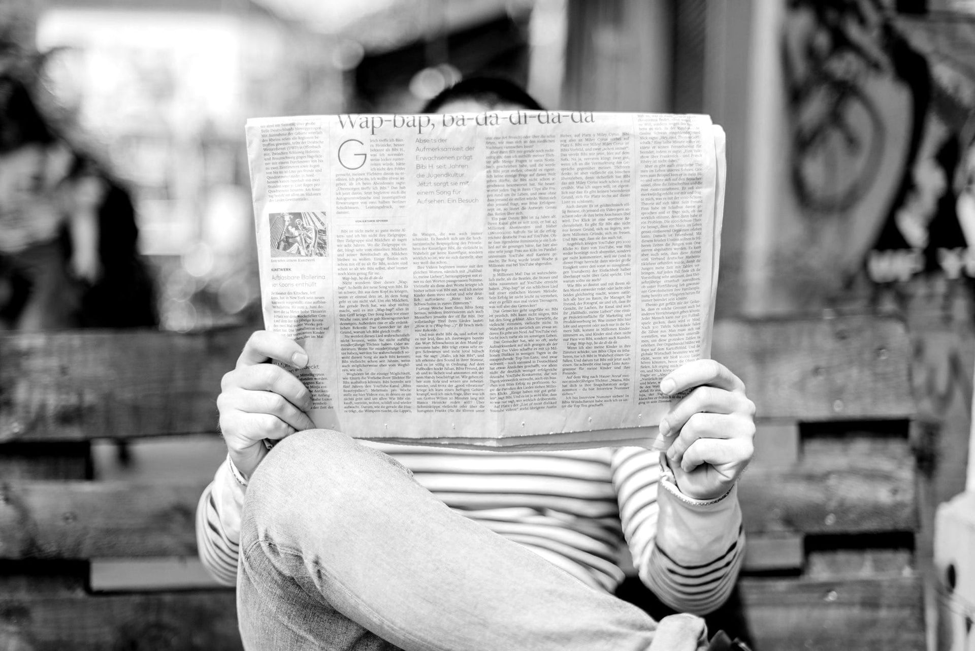  A man reads a newspaper on a park bench.