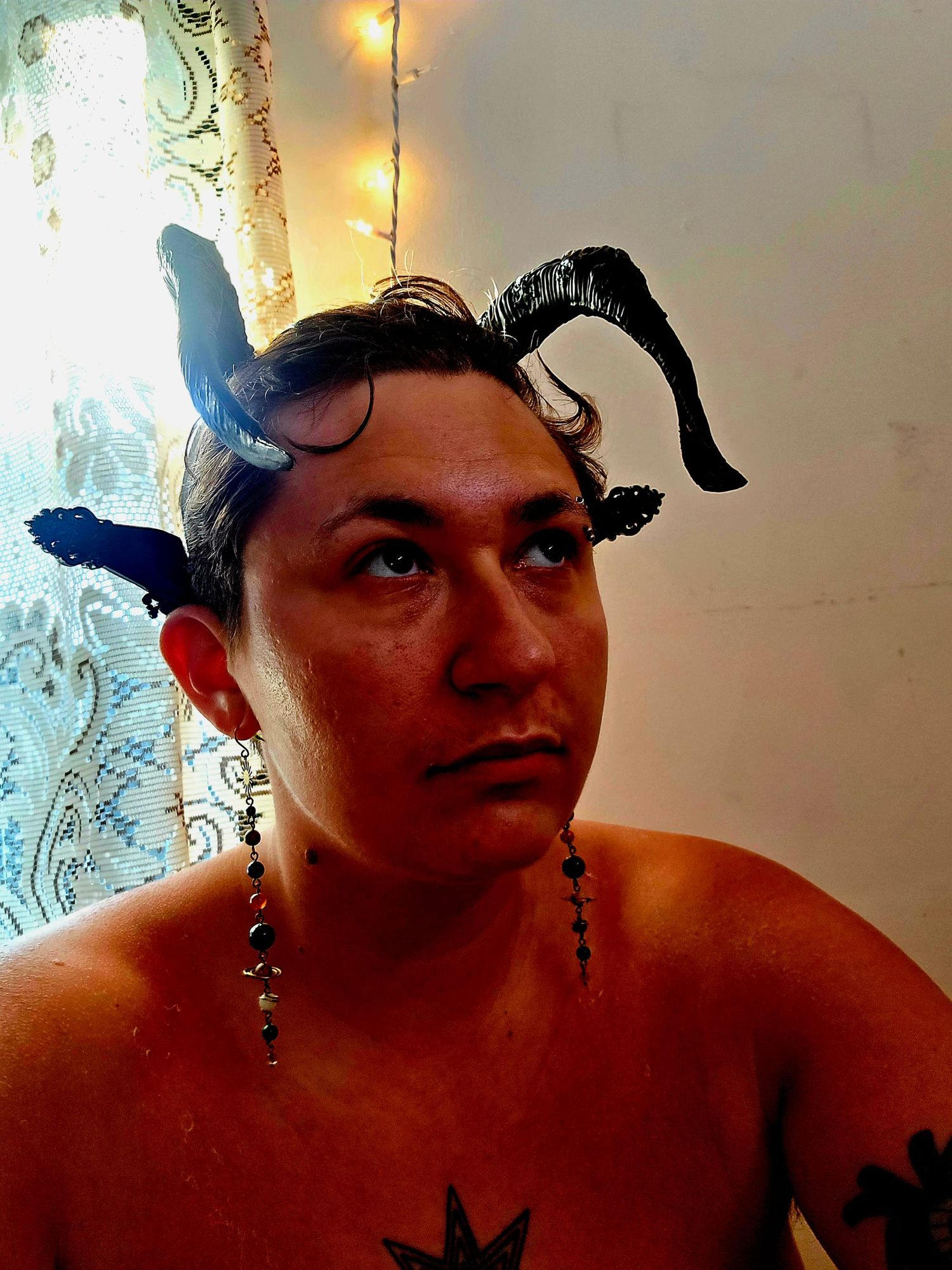 Photo of me, filtered to emphasize the deep red of my burned skin. You can see it blistering and peeling. I wear a black horned headband and dangling solar system earrings with each planet.
