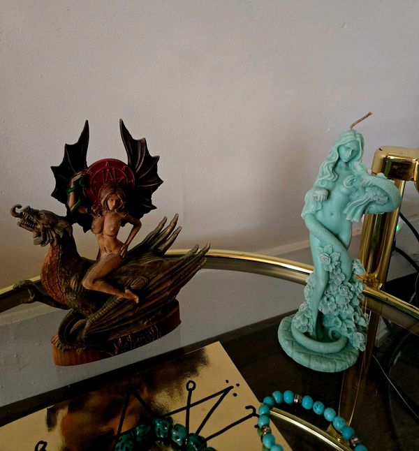 Two Astaroth statues sitting on her altar; one demonic on a dragon the other a blue flowery candle and entwined with a snake