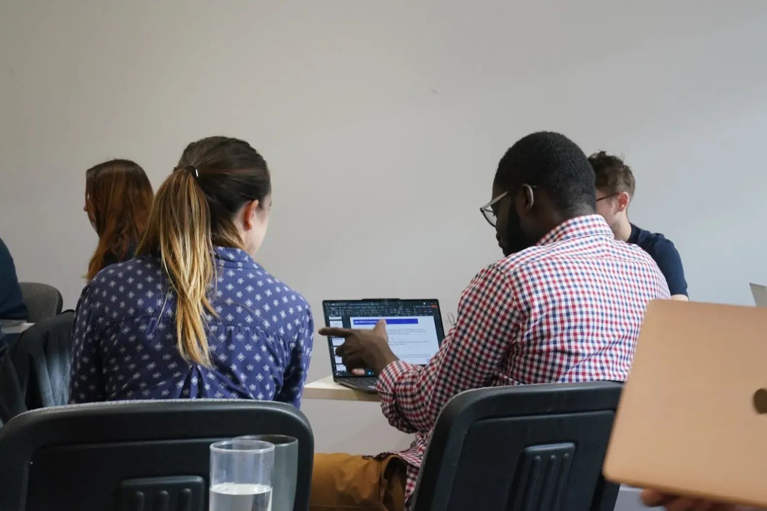 Pictured from behind, a man and a woman sit side by side working together on a laptop. 