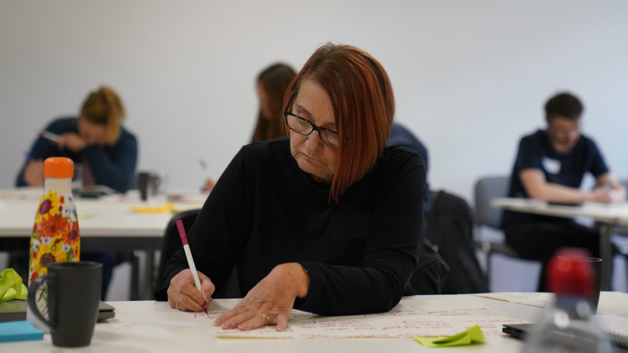 A woman writing on an A3 piece of paper during a workshop.