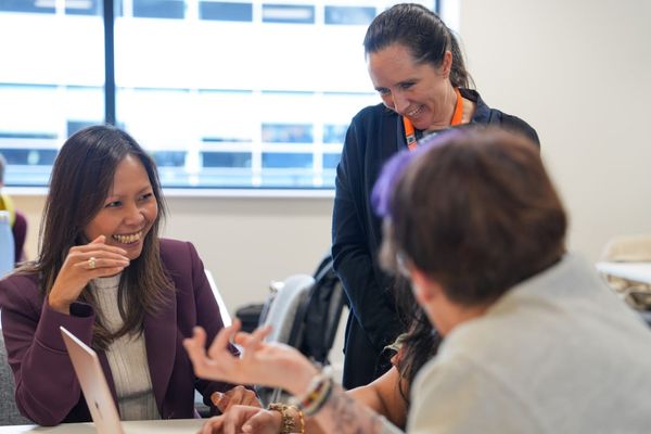 Two women smiling while speaking to a group in a professional setting. 