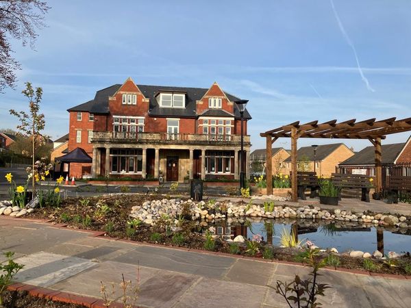 The exterior of the Caerphilly Miners Centre on a sunny day. In front is a pond, as well as some benches underneath a pergola.