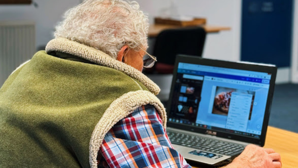 An elderly man using Canva on a laptop during a training session. 