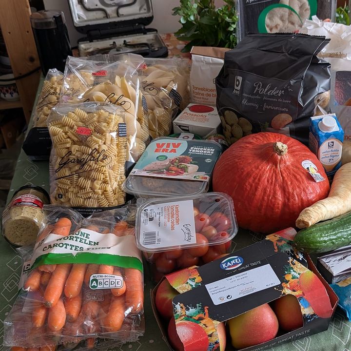 Groceries on a table, including a pumpkin, carrots, pasta packets, and more