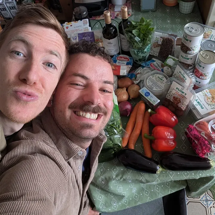 Ben and Sam posing by groceries bought from Colruyt, including a mix of vegetables, Plan't range items, and others.