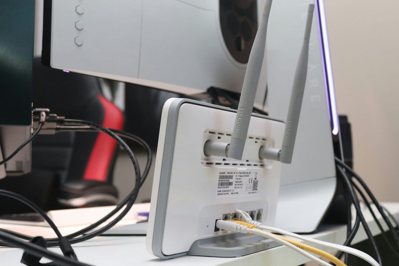 A white and grey wireless router with two external antennas stands on a white desk, connected to several ethernet - how to compare internet plans cables and power cords 
