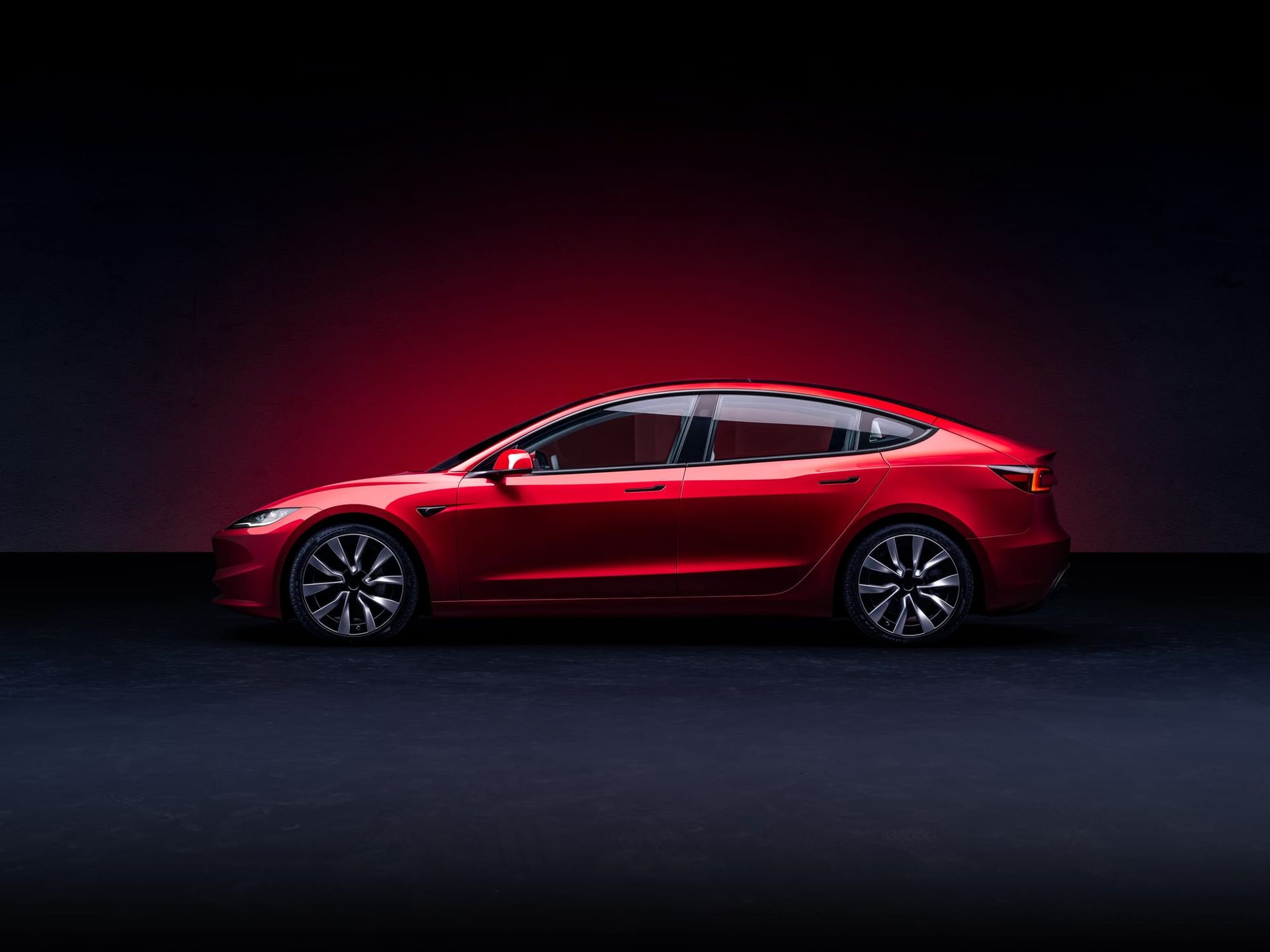 Red Tesla electric sedan photographed in profile against a dark studio background with red accent lighting - Tesla Full Self-Driving claims