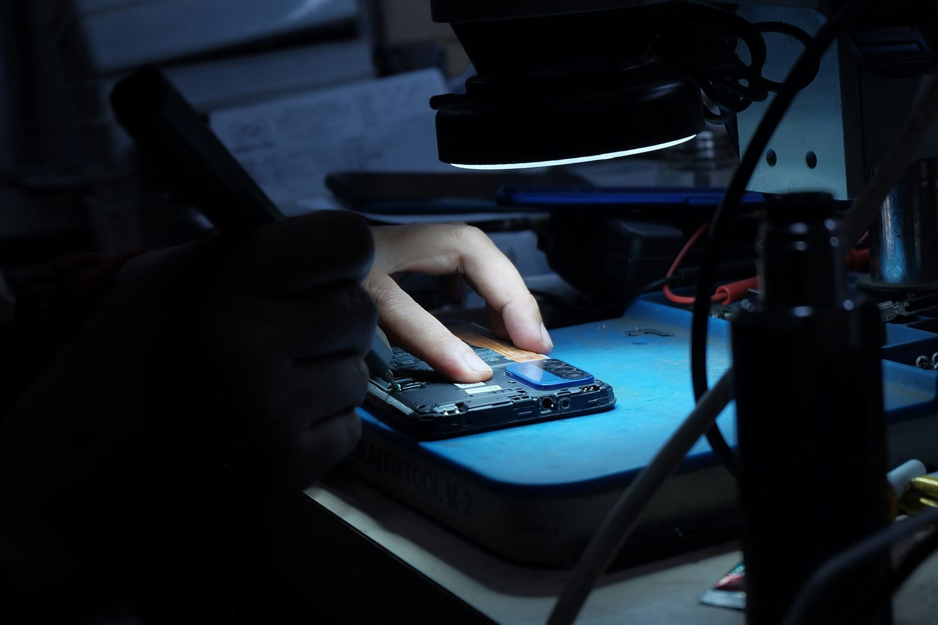 Technician examining an opened smartphone under a light at an electronics repair bench - extended warranty