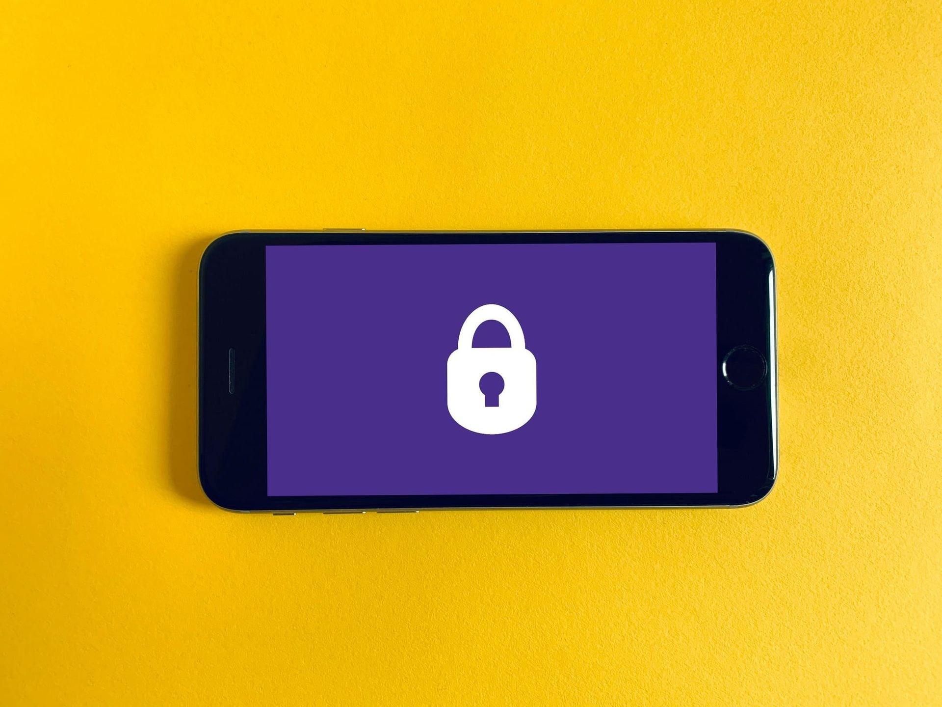 Smartphone lying horizontally on a yellow background, displaying a white padlock symbol on a purple screen - how to prevent SIM swapping