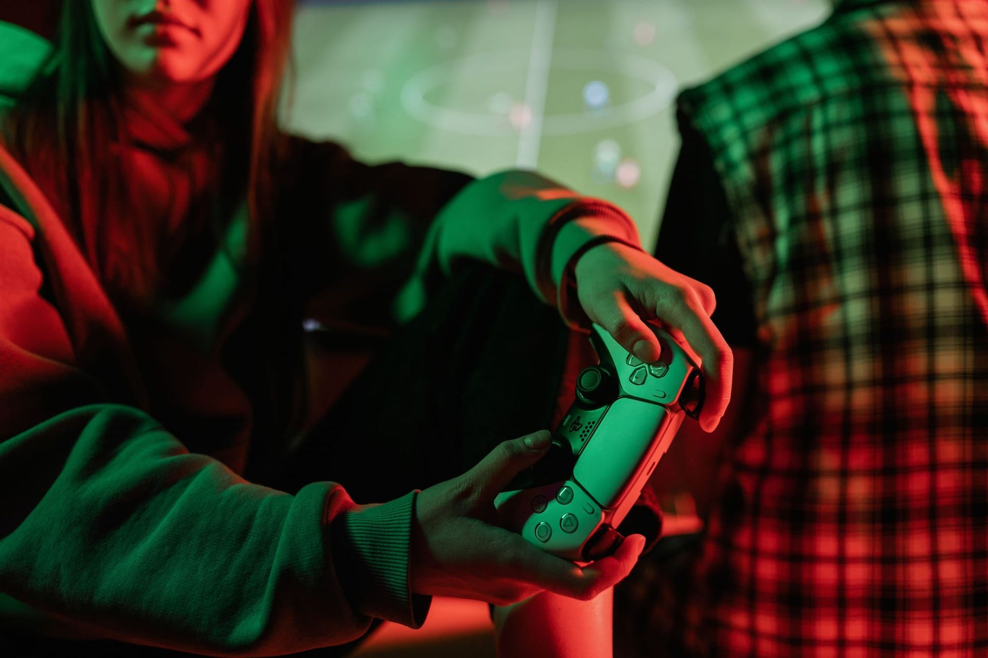 A person holding a video game controller in front of a screen in a colorfully lit room.